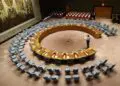 A wide-angle view of the United Nations Security Council chamber with empty seats arranged in a circular formation, symbolizing global diplomacy and decision-making.