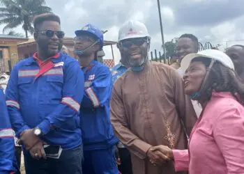 Representative Jeremiah Sokan Sr. in a brown kaftan greets a female engineer during a site visit in Grand Gedeh County, surrounded by local workers and project staff.