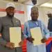 Two officials, CSA Director General Dr. Josiah Joekai Jr. and Afriland CEO Michel Doriand Pedie, hold signed partnership documents during the launch of the new salary advance and long-term loan program for Liberian civil servants