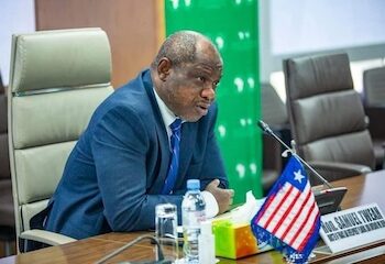 Former Finance Minister Samuel D. Tweah Jr. speaking at a meeting with the Liberian flag and EU flag on the table.