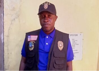 a man in a blue shirt, vest and a hat standing