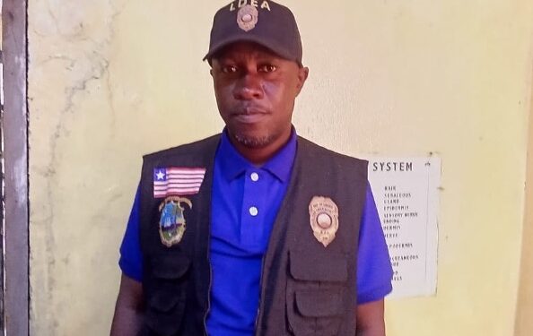 a man in a blue shirt, vest and a hat standing