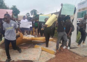 Students at the Lutheran University of Liberia protest by blocking an entrance with worn-out mattresses and holding handwritten signs, demanding better dormitory conditions and academic services.
