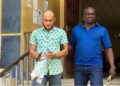 Peach Bility, escorted in handcuffs by a court officer, exits Criminal Court “C” in Monrovia following a pretrial hearing on drug and firearm charges.