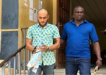 Peach Bility, escorted in handcuffs by a court officer, exits Criminal Court “C” in Monrovia following a pretrial hearing on drug and firearm charges.