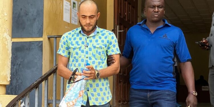 Peach Bility, escorted in handcuffs by a court officer, exits Criminal Court “C” in Monrovia following a pretrial hearing on drug and firearm charges.