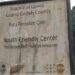 Faded signboard of Putu Pennoken Clinic and Youth Friendly Center in Grand Gedeh County, Liberia, surrounded by overgrown grass and an abandoned building