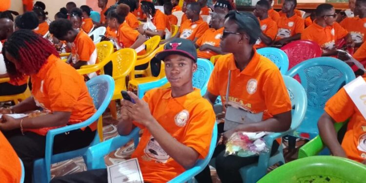 UBCAA computer literacy graduates in orange shirts seated during graduation ceremony in Gbarnga, Bong County