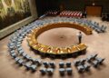 A wide-angle view of the United Nations Security Council chamber with empty seats arranged in a circular formation, symbolizing global diplomacy and decision-making.