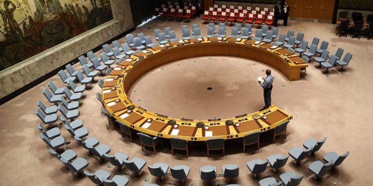 A wide-angle view of the United Nations Security Council chamber with empty seats arranged in a circular formation, symbolizing global diplomacy and decision-making.