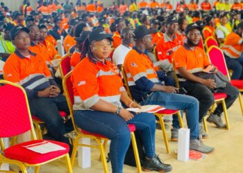 Liberian workers in orange uniforms seated during an ArcelorMittal Liberia employee event, showcasing local workforce engagement and company transparency.