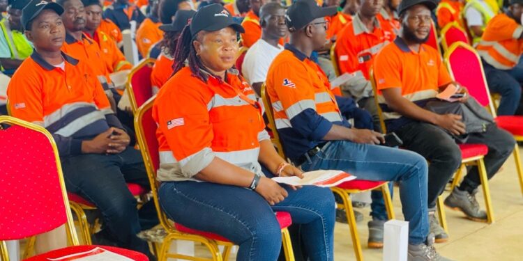 Liberian workers in orange uniforms seated during an ArcelorMittal Liberia employee event, showcasing local workforce engagement and company transparency.