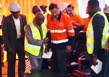 President Joseph Nyuma Boakai shakes hands with ArcelorMittal Executive Chairman Lakshmi Mittal during the inauguration of the $1.8 billion iron ore concentrator in Tokadeh, Nimba County, surrounded by executives and engineers in safety gear