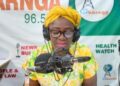 Bong County Superintendent Hawa Norris speaks into a microphone during a radio broadcast in Gbarnga, addressing misinformation and public protests.