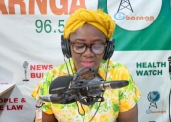 Bong County Superintendent Hawa Norris speaks into a microphone during a radio broadcast in Gbarnga, addressing misinformation and public protests.