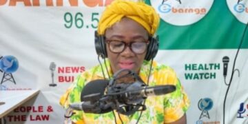 Bong County Superintendent Hawa Norris speaks into a microphone during a radio broadcast in Gbarnga, addressing misinformation and public protests.