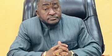 Ambassador Dee-Maxwell Saah Kemayah, Sr., seated behind a desk, hands clasped, wearing a striped traditional suit, addressing the public on Liberia’s election to the UN Security Council.”