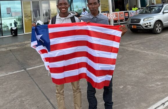 Douglas Sackor and Shaun Toteh hold a Liberian flag at the airport before departing for European football trials in Accra, Ghana.