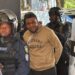 Capitol arson suspect John Nyanti in handcuffs escorted by heavily armed Liberian police officers, including a PSU officer in riot gear, outside the Temple of Justice in Monrovia.