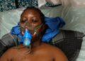 amesetta Kugmeh lying on a hospital bed wearing an oxygen mask, visibly weak and receiving treatment before her death in May 2025