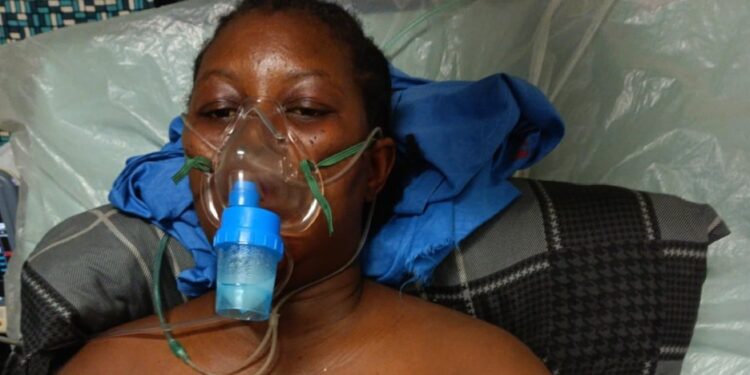 amesetta Kugmeh lying on a hospital bed wearing an oxygen mask, visibly weak and receiving treatment before her death in May 2025