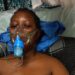 amesetta Kugmeh lying on a hospital bed wearing an oxygen mask, visibly weak and receiving treatment before her death in May 2025
