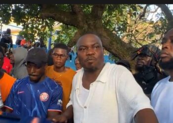 CDC National Treasurer Janga A. Kowo addresses a crowd of supporters under a tree in Monrovia, flanked by young men and party loyalists during a press engagement on the detention of opposition lawmakers