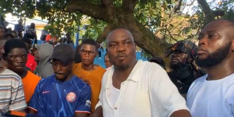 CDC National Treasurer Janga A. Kowo addresses a crowd of supporters under a tree in Monrovia, flanked by young men and party loyalists during a press engagement on the detention of opposition lawmakers