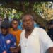 CDC National Treasurer Janga A. Kowo addresses a crowd of supporters under a tree in Monrovia, flanked by young men and party loyalists during a press engagement on the detention of opposition lawmakers