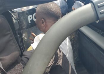 CDC Chairman Janga Kowo seated in the back of a police pickup truck, partially obscured by a riot shield and surrounded by police officers during his arrest in Monrovia.