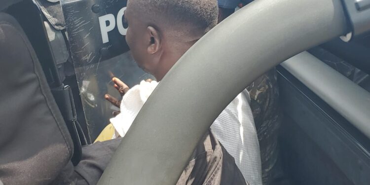 CDC Chairman Janga Kowo seated in the back of a police pickup truck, partially obscured by a riot shield and surrounded by police officers during his arrest in Monrovia.