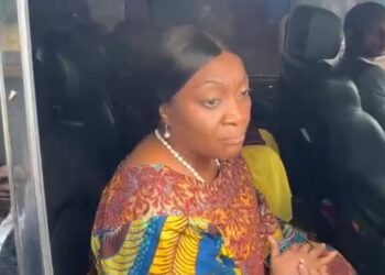 Former Vice President Jewel Howard-Taylor sits inside a vehicle, speaking to reporters after visiting jailed lawmakers at the Monrovia Central Prison, wearing a colorful traditional outfit and pearl necklace.