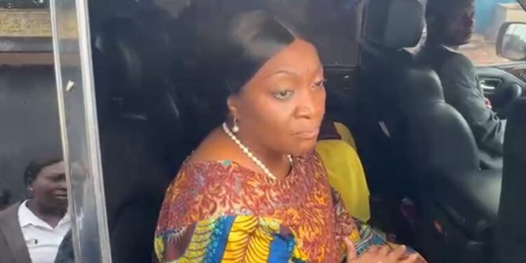 Former Vice President Jewel Howard-Taylor sits inside a vehicle, speaking to reporters after visiting jailed lawmakers at the Monrovia Central Prison, wearing a colorful traditional outfit and pearl necklace.