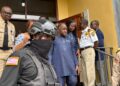 Ambassador Dee-Maxwell Saah Kemayah exits a courthouse in Monrovia surrounded by security personnel, including an armed officer in tactical gear and uniformed court officers, following his arrest in connection with a corruption investigation.