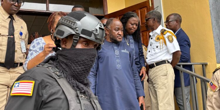 Ambassador Dee-Maxwell Saah Kemayah exits a courthouse in Monrovia surrounded by security personnel, including an armed officer in tactical gear and uniformed court officers, following his arrest in connection with a corruption investigation.