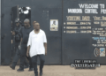CDC Chairman Janga Augustus Kowo walks out of the Monrovia Central Prison after his release, escorted by security personnel, with the prison gate and visitation schedule visible in the background