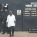CDC Chairman Janga Augustus Kowo walks out of the Monrovia Central Prison after his release, escorted by security personnel, with the prison gate and visitation schedule visible in the background