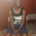 Lawrence K. Williams, suspect in the alleged vehicular attack on Unity Party supporters, seated in a holding area wearing a black sleeveless shirt and blue shorts, hands clasped, awaiting trial amid stalled proceedings