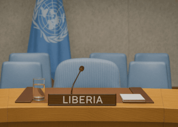 Liberia’s designated seat at the United Nations Security Council, featuring a wooden desk with a nameplate labeled “LIBERIA,” a microphone, a glass of water, documents, and several light blue chairs in the background, with the UN flag hanging behind.