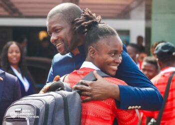 LFA president Mustapha Raji embraces a smiling player from the Liberia Women’s National Football Team as they return from Mauritania after finishing third at the 2025 WAFU Zone A Women’s Cup. Four players, proudly wearing medals, pose with Quamie in a celebratory photo.