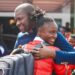 LFA president Mustapha Raji embraces a smiling player from the Liberia Women’s National Football Team as they return from Mauritania after finishing third at the 2025 WAFU Zone A Women’s Cup. Four players, proudly wearing medals, pose with Quamie in a celebratory photo.