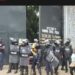Riot police stand guard at the entrance of Monrovia Central Prison as a group of officers and civilians look on during the detention of lawmakers accused in the Capitol Building arson case
