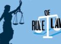 Illustration of Lady Justice holding balanced scales and a sword, symbolizing fairness and the rule of law. Next to her is a stylized text graphic reading “Rule of Law,” with the word “Law” forming part of a scale, set against a light blue background.