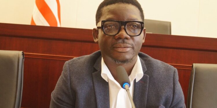 Tarnue N. Jeke, nominee for Deputy Minister for Administration at Liberia’s Ministry of Commerce, seated at a confirmation hearing before the Senate Committee, wearing a dark blazer and glasses.