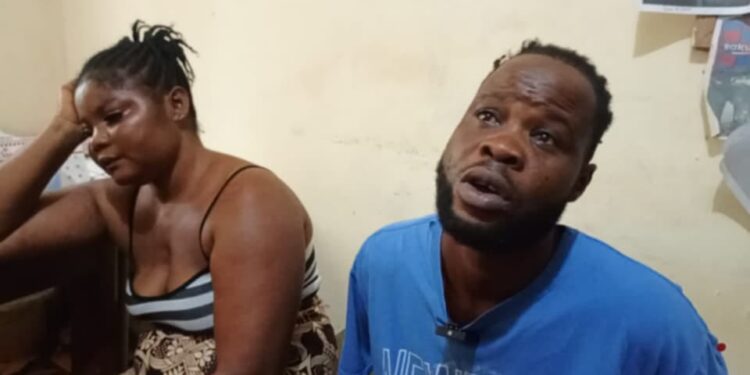 A man and a woman, identified as Zarwu Kennedy, 32, and Princess Varnah, 30, sit indoors after their arrest in Bong County, Liberia, for alleged drug trafficking. The woman appears distressed, resting her head on her hand, while the man looks upward, speaking.
