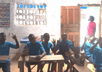 Deaf students seated in a dimly lit classroom at the Gbarnga Central School of the Deaf in Bong County, Liberia, signaling their enthusiasm for learning despite a lack of government support