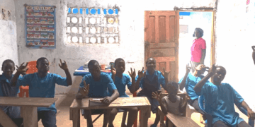 Deaf students seated in a dimly lit classroom at the Gbarnga Central School of the Deaf in Bong County, Liberia, signaling their enthusiasm for learning despite a lack of government support