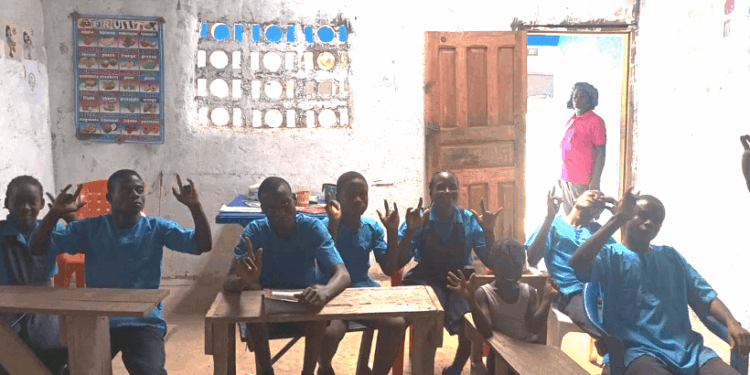 Deaf students seated in a dimly lit classroom at the Gbarnga Central School of the Deaf in Bong County, Liberia, signaling their enthusiasm for learning despite a lack of government support