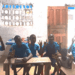 Deaf students seated in a dimly lit classroom at the Gbarnga Central School of the Deaf in Bong County, Liberia, signaling their enthusiasm for learning despite a lack of government support