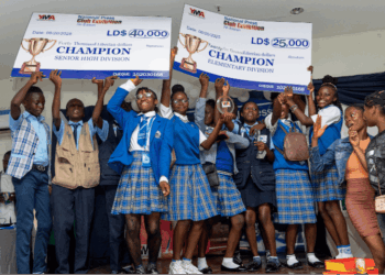Students from Kings and Queens International School celebrate winning first place in the YMA National Press Club Exhibition, holding L$25,000 and L$40,000 championship checks on stage